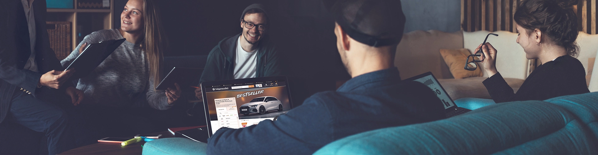 Mitarbeitende diskutieren Ideen, während die Felgenoutlet-Website auf einem Laptop angezeigt wird.